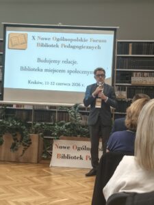 Mężczyzna w garniturze i okularach mówi do mikrofonu.