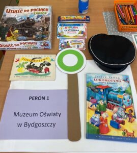 Ułożone na stole: czapka kolejarza, lizak, gra planszowa, książka i dyplom.
