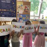 Czworo dzieci zasłania sobie twarze kartkami - na kartkach hasła "Cała Polska Czyta Dzieciom".