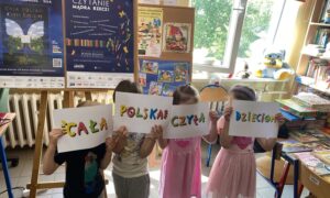 Czworo dzieci zasłania sobie twarze kartkami - na kartkach hasła "Cała Polska Czyta Dzieciom".