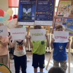 Pięcioro dzieci zasłania sobie twarze kartkami z hasłem "XXV Ogólnopolski Tydzień Czytania Dzieciom".