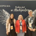 Trzy kobiety pozują do zdjęcia na ściance z białymi skrzydłami.