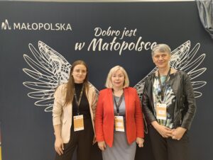 Trzy kobiety pozują do zdjęcia na ściance z białymi skrzydłami.