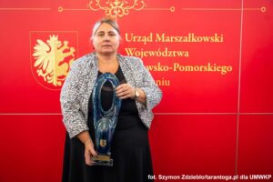 Blondwłosa kobieta trzyma szklane trofeum.