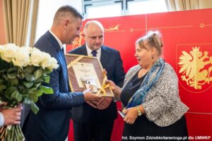 Dwóch mężczyzn wręcza kwiaty kobiecie.