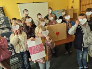 Grupa dzieci z zasłoniętymi serduszkami twarzami, stoją wokół drewnianej skrzynki.